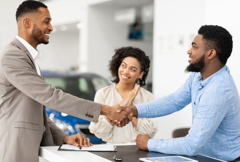 Two men shake hands as woman looks on smiling.